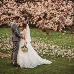 Bride and groom kiss under blooming magnolia tree.