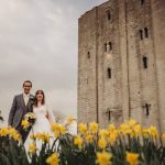 Couple poses by castle with daffodils in foreground.