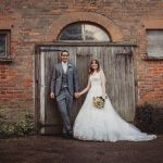 Bride and groom holding hands by rustic doorway.