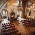 Medieval castle hall with chairs and chandeliers.