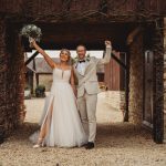 Bride and groom celebrating under rustic archway.