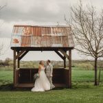 Bride and groom under rustic shelter in countryside