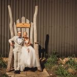 Couple sitting on large wooden chair, wedding attire.