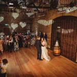 Wedding couple dancing in rustic venue with guests.