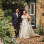 Bride and groom walking in garden, holding hands.