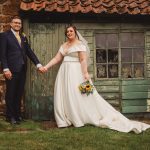 Bride and groom holding hands outside rustic building.