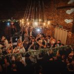 Guests dancing at lively wedding reception in rustic venue.