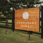 Curradine Barns wooden sign in a garden setting.