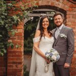 Smiling couple in wedding attire by brick archway