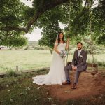 Wedding couple on swing under tree in garden.