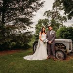 Bride and groom posing by vintage tractor outdoors.