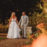 Bride and groom walking in autumn garden.