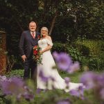 Bride and groom in garden, purple flowers foreground.