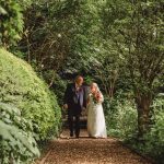 Bride and groom walking in lush garden path.