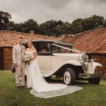 Bride and groom stand by vintage wedding car.