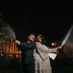 Couple celebrating wedding with champagne spray at night.