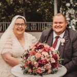 Smiling couple with wedding bouquet outdoors.