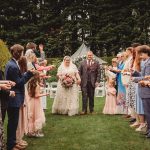 Bride and groom walk through celebrating guests outdoors.