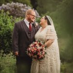 Bride and groom smiling in garden setting.