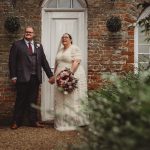 Wedding couple holding hands by rustic doorway.