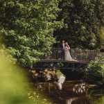 Couple on bridge surrounded by lush greenery.