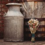 Vintage milk churn and flowers beside wooden barrel