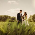 Bride and groom standing in sunlit field