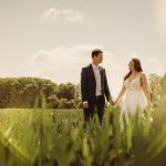 Bride and groom holding hands in sunny field.