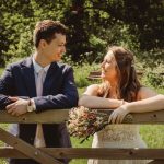 Couple leaning on wooden gate in sunny garden.