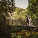 Wedding couple standing on charming garden bridge.