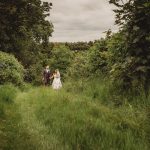 Bride and groom walking through lush green path.