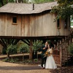 Newlyweds outside a rustic wooden treehouse in nature.