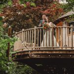 Couple on wooden treehouse balcony, surrounded by nature.