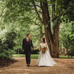 Bride and groom walking in a wooded garden.