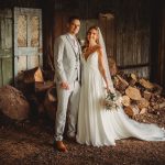 Couple in wedding attire smiling, rustic wooden backdrop.