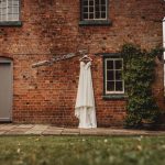 White wedding dress hanging on brick cottage wall.