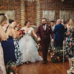 Newlyweds walk down aisle, guests applauding happily.