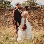 Wedding couple in garden near brick wall.