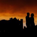 Silhouetted couple at sunset by historic building.