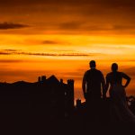 Couple silhouetted against dramatic sunset sky.