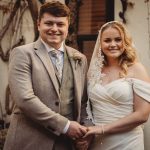 Smiling bride and groom hold hands outdoors.