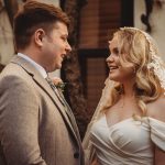 Bride and groom smiling at each other outdoors.