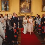 Bride walking down aisle in decorated ceremony room.