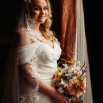 Bride holding bouquet by window.