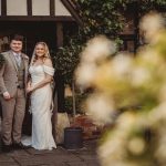 Bride and groom smiling at rustic venue entrance.