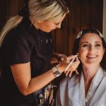 Woman applying makeup to smiling bride