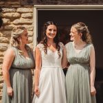 Bride and bridesmaids smiling outside rustic building