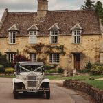 Vintage white car outside stone cottage.