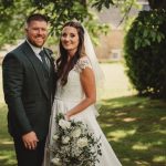 Smiling wedding couple outdoors with bouquet.