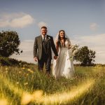 Bride and groom walking in sunny field